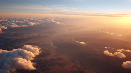 Obraz premium A breathtaking aerial view showcasing expansive mountains and soft clouds illuminated by a warm sunset glow.