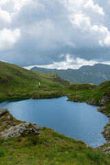 Mountain lake under dramatic clouds in the Fagaras Mountains, Romania. Summer scenery with green slopes and clear water.