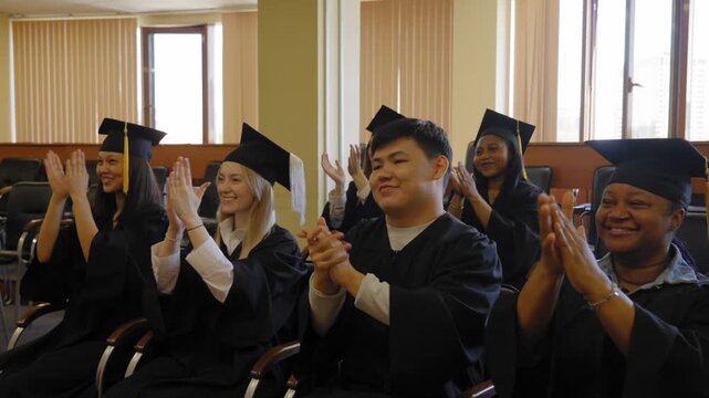 Graduates sit on a bench, listen to the speech and applaud. 