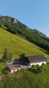 Vertical, aerial: Laimeralm mountain hut Inn above Lake Wolfgang at sunset with golden hour light in Austria, orbit drone shot