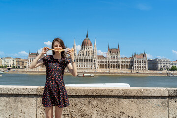 Obraz premium Woman Enjoying Kürtőskalács in Front of Budapest Parliament