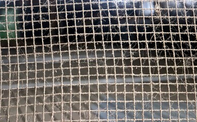A damaged wire fence covered in dust and cobwebs. A rusty iron wire fence with holes, old, and...