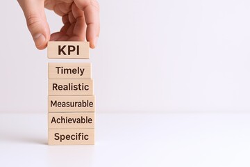 Hand stacking wooden blocks labeled KPI Timely Realistic Measurable Achievable Specific for Business Progress.