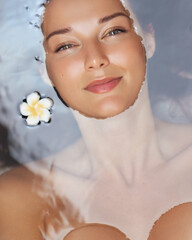 Smiling Woman Lying In Water With Plumeria In Regular Spa Bath Setting