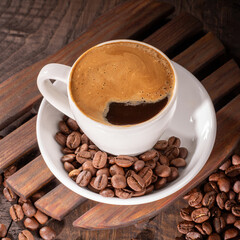 Delicious cup of coffee topped with froth and enveloped by coffee beans