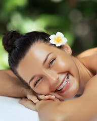 Smiling Woman Lying on Massage Table With Flower in Hair at Spa