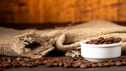 A cup overflowing with coffee beans and spilled beans on kitchen table