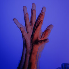 Double exposure of raised hands in motion with surreal blue and red lighting