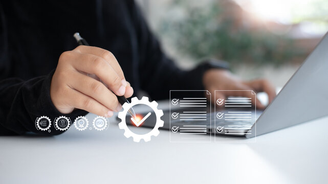 Hand pointing to a checkmark on the gear icon with a checklist and ISO symbols. Concept of quality assurance, compliance, standardization, and business process automation.