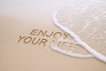 Fototapeta premium Enjoy Your Life Written in Sand on Beach with Ocean Wave at Shore.