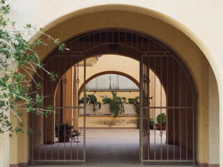 Fototapeta premium Archway with Potted Plants and Metal Fence – Italian Apartment Building in Golfo Aranci, Sardinia, Horizontal Photo