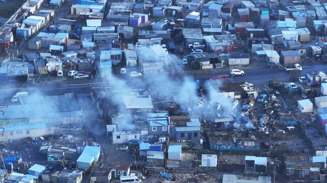 Close-up of smoke rising from dense housing in Cape Town's informal settlement of Du Noon, showing tight streets and rudimentary tin shack housing in this poor area.