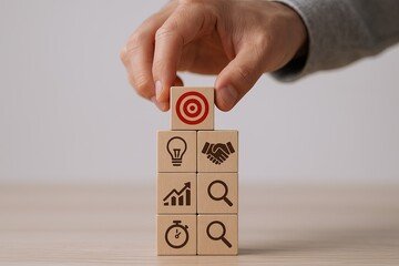 Hand stacking wooden blocks with icons representing goal achievement teamwork and innovation.