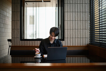 Casual professional workspace featuring a man smiling at his laptop with a cup of coffee