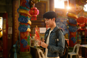 A young traveler closes his eyes in peaceful prayer, holding incense sticks, Spiritual Moment at a...