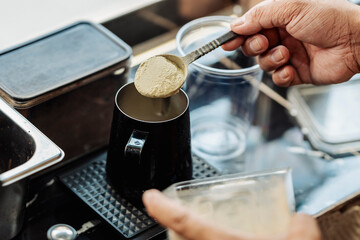 Barista adds a spoonful of green matcha powder to a metal pitcher while preparing a matcha-based drink at a coffee stall.