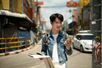 A young traveler cross references a paper map and smartphone on a busy city street