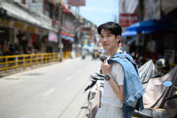Portrait of A stylish young man with a denim jacket over his shoulder poses confidently on a...