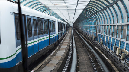 Blue and white metro train traveling through a modern covered tunnel with parallel tracks, electric...