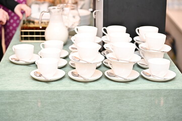 Stacked white porcelain cups with spoons on a catering table