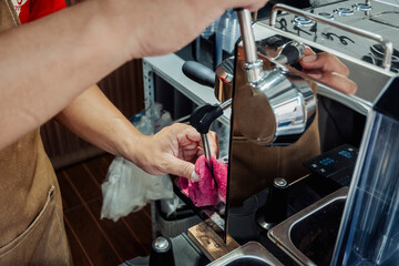 Barista wipes down the top of a shiny espresso machine with a red cloth, maintaining cleanliness in a busy café setting.
