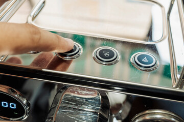 Barista finger presses button on shiny espresso machine to start brewing process during coffee preparation in modern café.