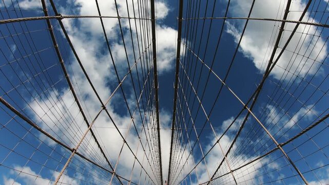Panoramic architectural view of Brooklyn bridge cables against a clear blue sky and Manhatttan skyscrapers in New York at background