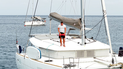 Morning on a yacht. Fitness exercises on the roof of a catamaran. A man doing exercises during a sea voyage. Warm-up exercises, morning activity. Exercises with a power rubber band