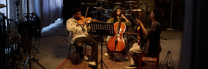 Three musicians, two Black males and one Latin female, playing violin, cello, and guitar together...