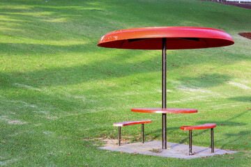 red picnic table and umbrella in park against green lawn