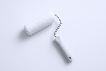 Obraz premium Close-up of a small paint roller with white fuzzy fabric and metal frame on white background.