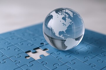 Close up of glass globe on blue puzzle pieces with missing piece on light background.