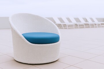 Modern white wicker outdoor chair with blue cushion on tiled patio with lounge chairs.