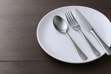 Empty white plate with stainless steel spoon fork and knife on wooden surface.