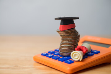 Graduation mortarboard university hat, stack coins, calculator, red ladder on wooden table white wall background. Financial planning for education, student loan or debt, scholarship and so on concept.
