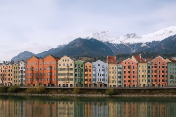 Fototapeta premium Colorful traditional European houses along a fjord with snow-capped mountains in the background.