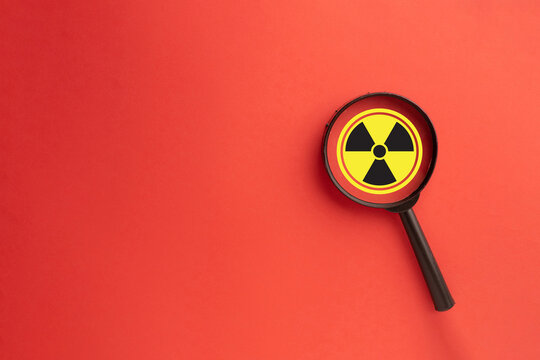 Radiation danger and hazard warning concept. A magnifying glass over a radioactive symbol on a red alert background with copyspace. Highlighting the risk of toxic materials,environmental protection. - Powered by Adobe