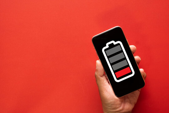 Low battery warning concept.,A hand holding a mobile phone with a red empty power indicator on red background with copyspace idea for human burnout, stress, and exhaustion.