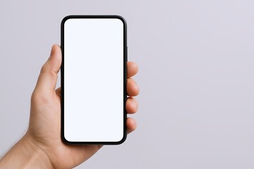 Hand holding smartphone with blank screen in portrait orientation in front of plain background.