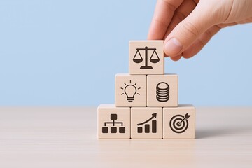 Hand stacking wooden blocks with business, finance, growth, and success symbols on a light blue background.