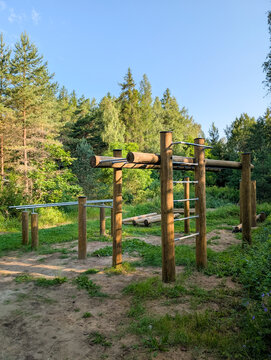 A wooden workout and calisthenics ground with pull-up and parallel bars, installed in a summer forest for fitness activities.