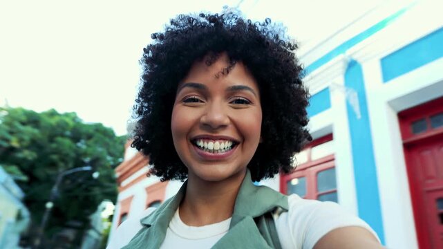 Young Black woman laughing while taking a selfie with her smartphone in a colorful colonial street. Joyful travel moment in a vibrant Latin American city.