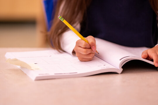 Close-up of student hand writing notes in open notebook with number 2 pencil. Shows active learning and study process in educational setting.
