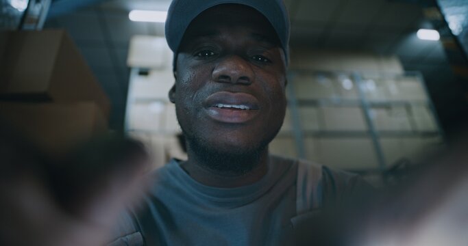 POV from Phone Screen: African American Employee Using Smartphone, Scrolling and Chatting in Social Networks. In the Background, Diverse Loaders Working in Logistics Distribution Warehouse at Night.