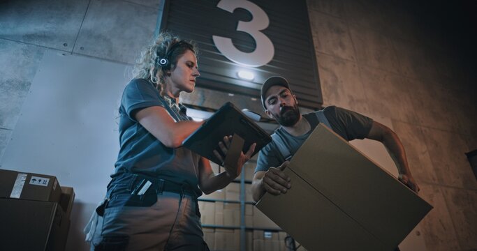 Female Manager Scanning Parcels with Barcode Scanner, Using Digital Tablet. Diverse Employees Carrying Cardboard Boxes from Logistics Distribution Warehouse at Night. Online Orders, Goods, Delivery.