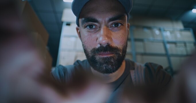 POV from Smartphone Screen: Male Worker Using Phone, Chatting in Social Networks. In the Background, Diverse Employees Carrying Cardboard Boxes with Online Orders in Logistics Warehouse at Night.