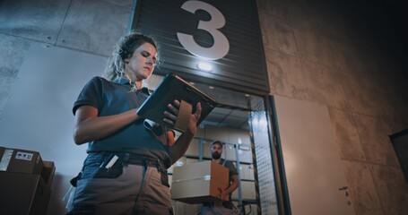 Female Manager Scanning Parcels with Barcode Scanner, Using Digital Tablet. Diverse Employees Carrying Cardboard Boxes from Logistics Distribution Warehouse at Night. Online Orders, Goods, Delivery.