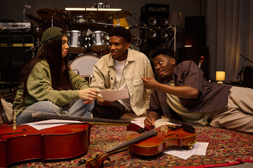 Three young adults, two Black men and one Hispanic woman, sitting and lying on carpeted floor in...