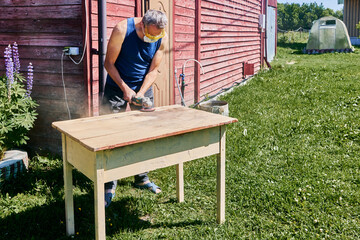 Using angle grinder for sanding tabletop, craftsman wearing respirator and safety glasses working...