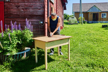 Using angle grinder for sanding wooden table, homeowner working on backyard project surrounded by...